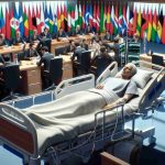 High-definition realistic representation of an unnamed politician lying in a hospital bed during an international conference. This figure is in bed looking unwell but alert, with medical equipment around him indicating that he is monitored. International flags hang low in the background, suggesting that the hospital milieu has been partially transformed into a conference room. Delegates from different countries, some visibly worried, are scattered around the room discussing urgent matters.